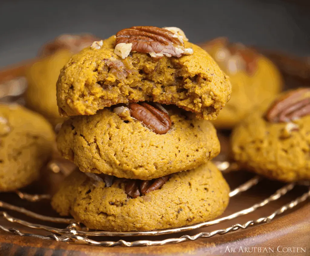 Golden Pumpkin Pecan Cookies with a crunchy pecan topping and a soft, moist center on a rustic wooden surface.