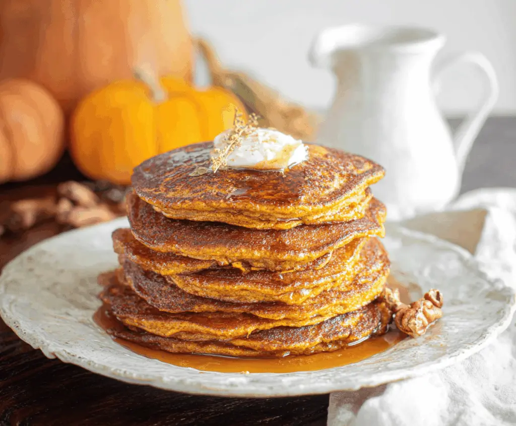 Delicious homemade sourdough pumpkin pancakes topped with whipped cream and cinnamon, served on a rustic plate for a cozy breakfast.