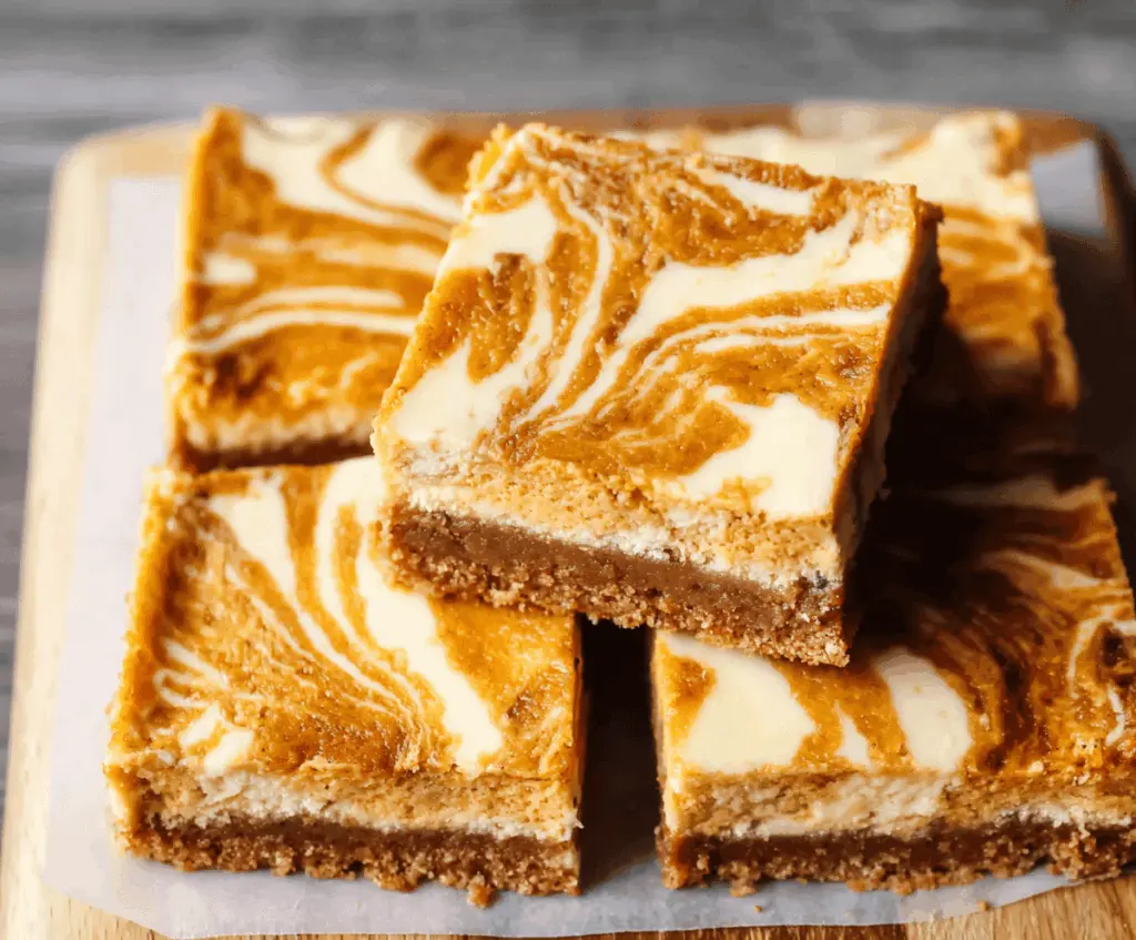 Creamy pumpkin swirl cheesecake bars topped with a cinnamon graham cracker crust, perfect for fall desserts.
