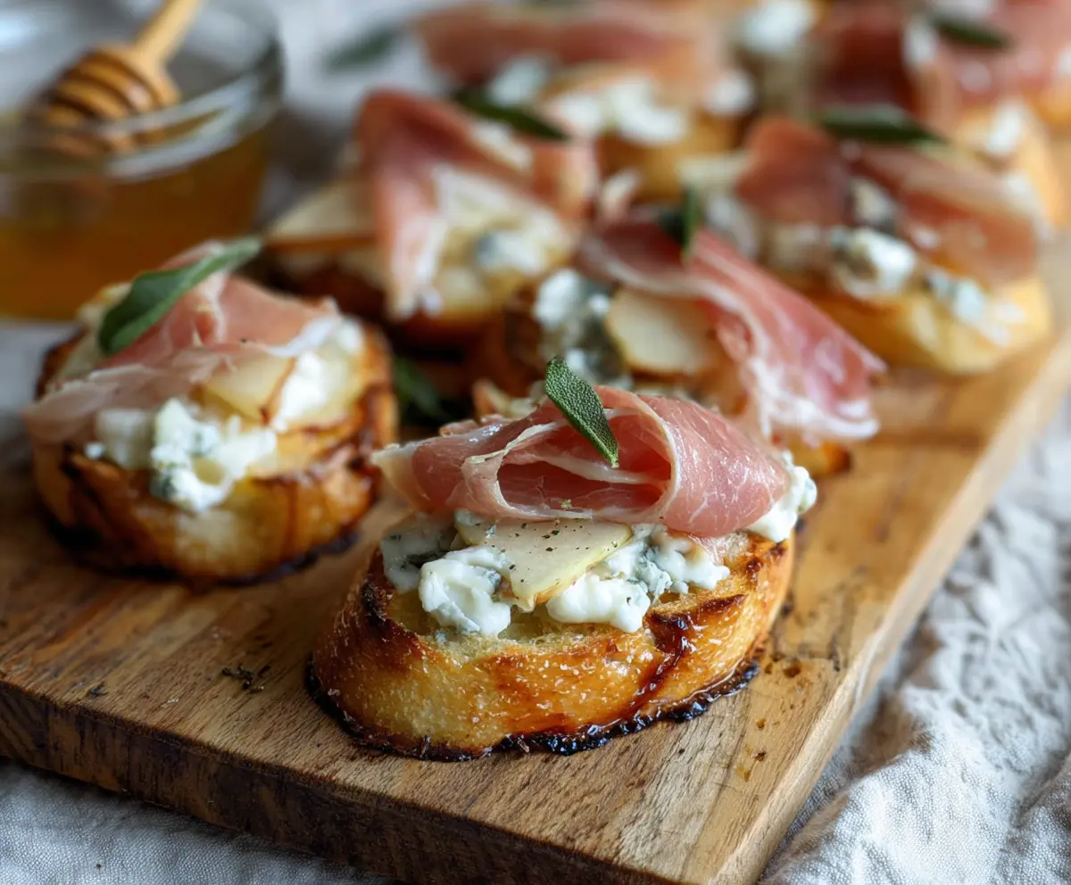 Delicious Prosciutto Pear Gorgonzola Crostini topped with fresh herbs and a drizzle of honey.