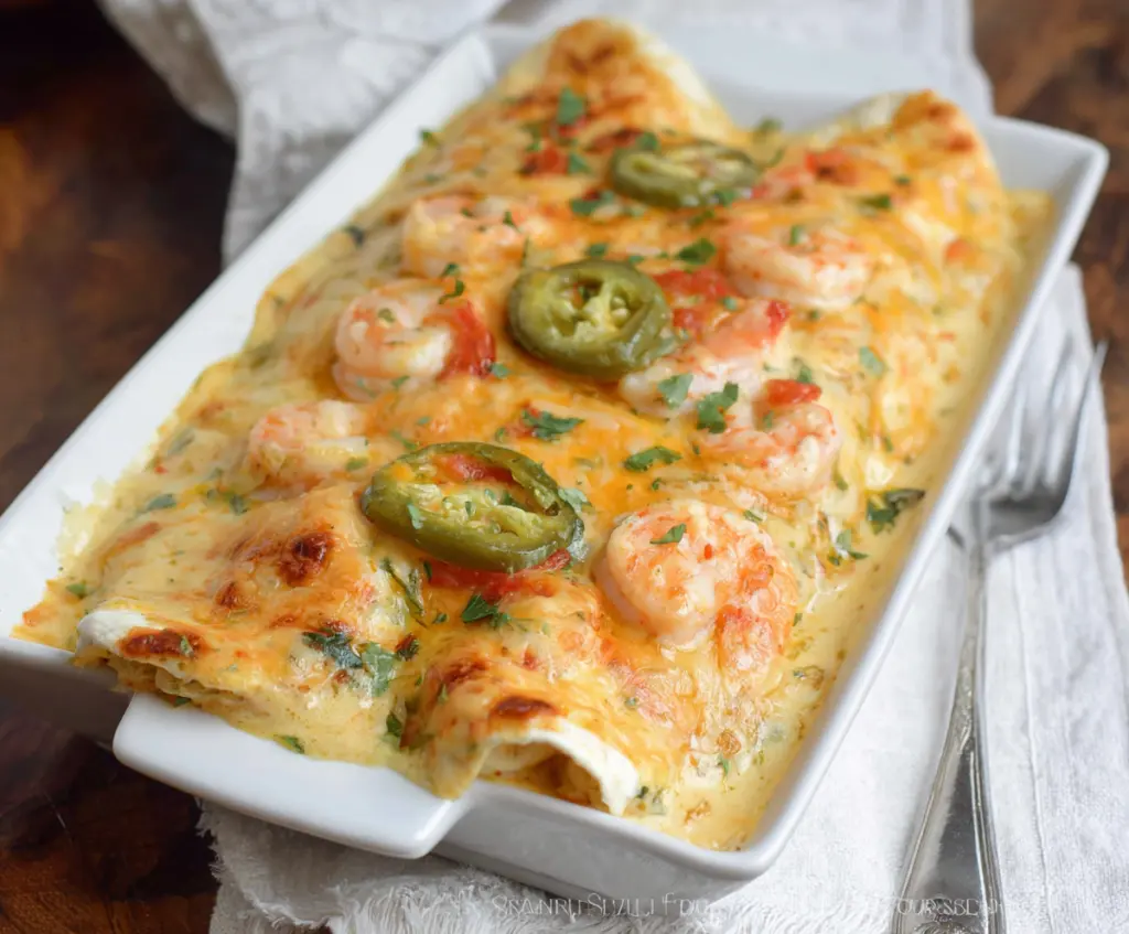 Delicious creamy shrimp enchiladas garnished with fresh herbs on a white plate.