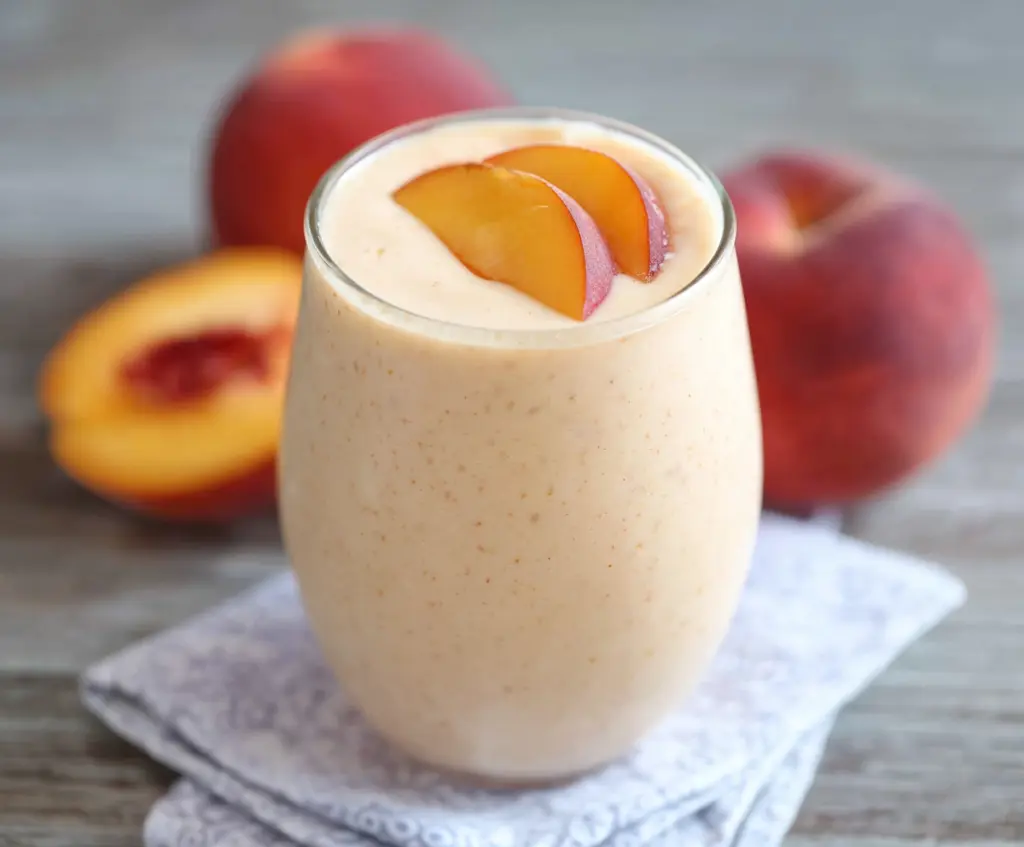 Refreshing peach protein smoothie in a clear glass with ice and fresh peach slices for a healthy breakfast.