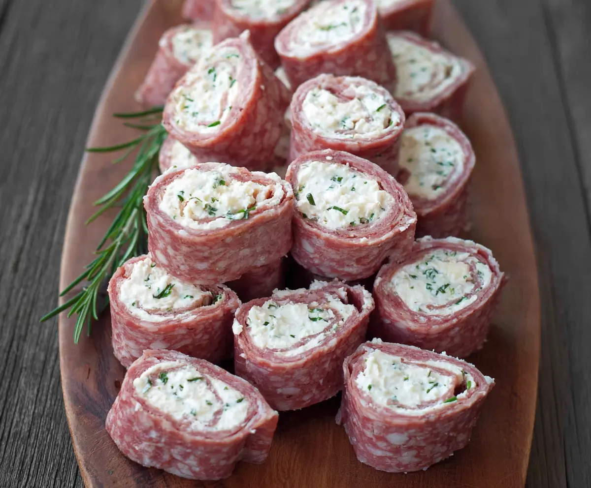 Delicious salami and cream cheese roll ups garnished with herbs on a wooden cutting board.