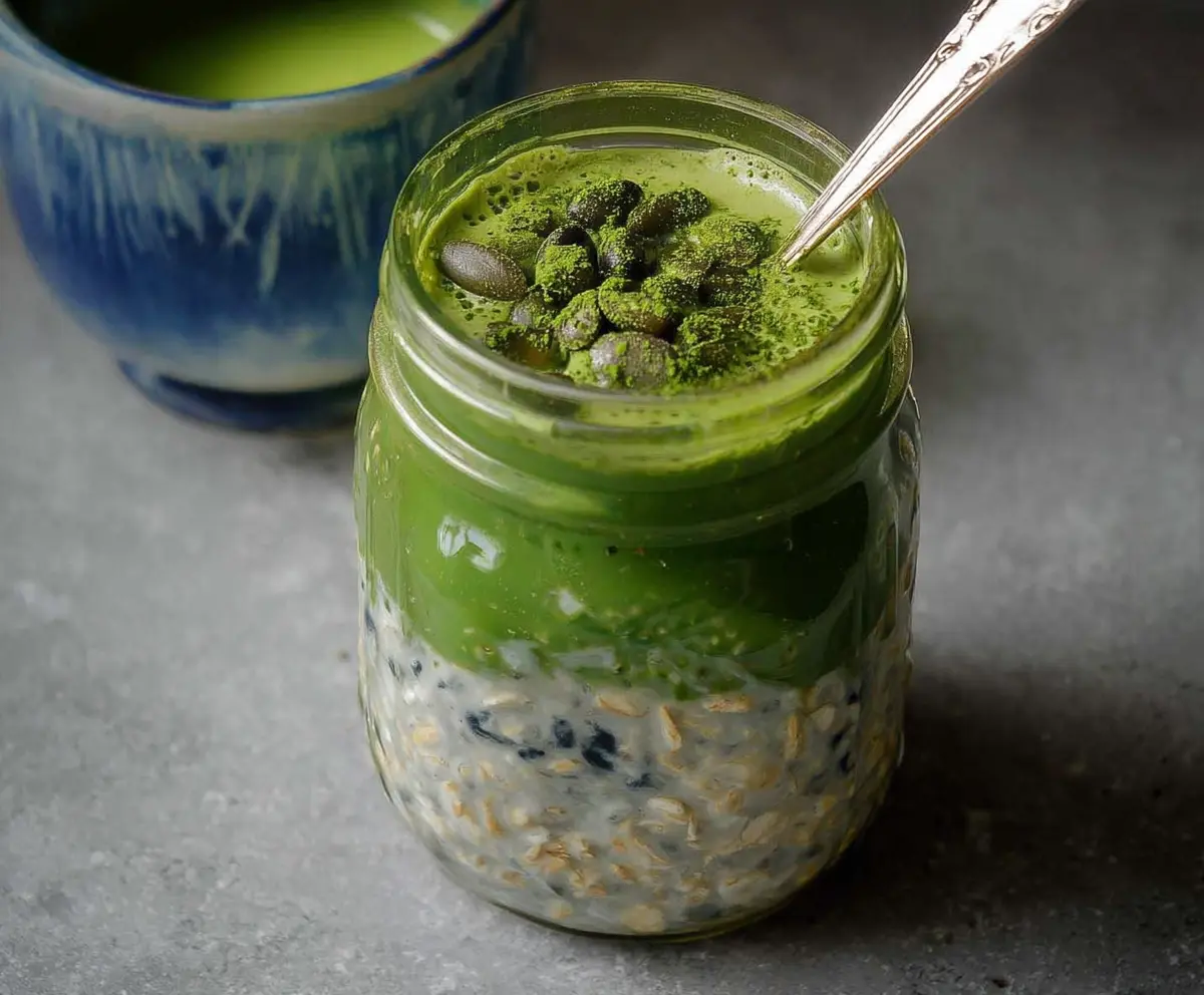 Creamy Matcha Latte Overnight Oats in a glass jar topped with fresh green matcha powder.