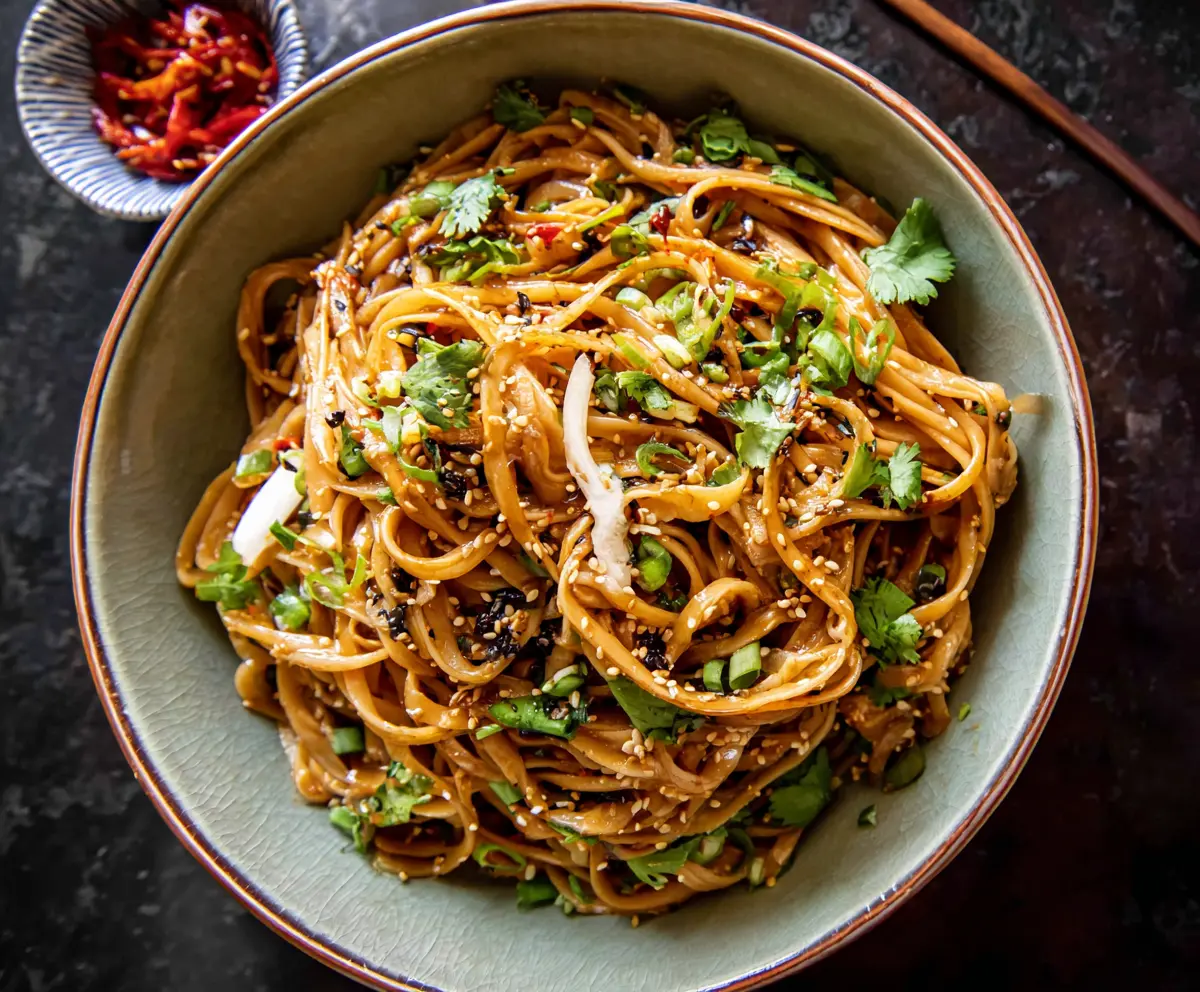 Delicious sesame garlic noodles served in a bowl, garnished with fresh herbs and sesame seeds.
