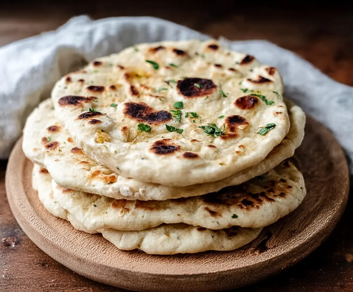 Homemade sourdough discard naan bread on a rustic wooden table, showing golden-brown crust and soft interior.