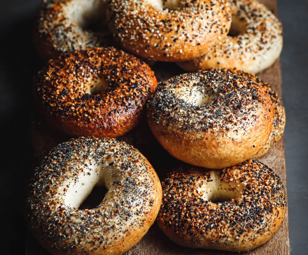 Golden-brown New York-style bagels topped with sesame seeds on a rustic wooden table.