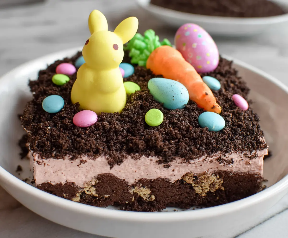 Easter Dirt Cake in a clear glass dish topped with colorful sprinkles and chocolate bmed eggs for festive dessert