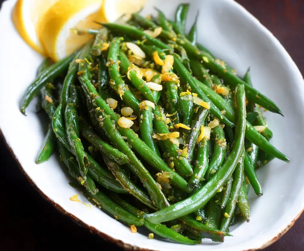 Vibrant lemon green beans garnished with fresh herbs on a white plate.