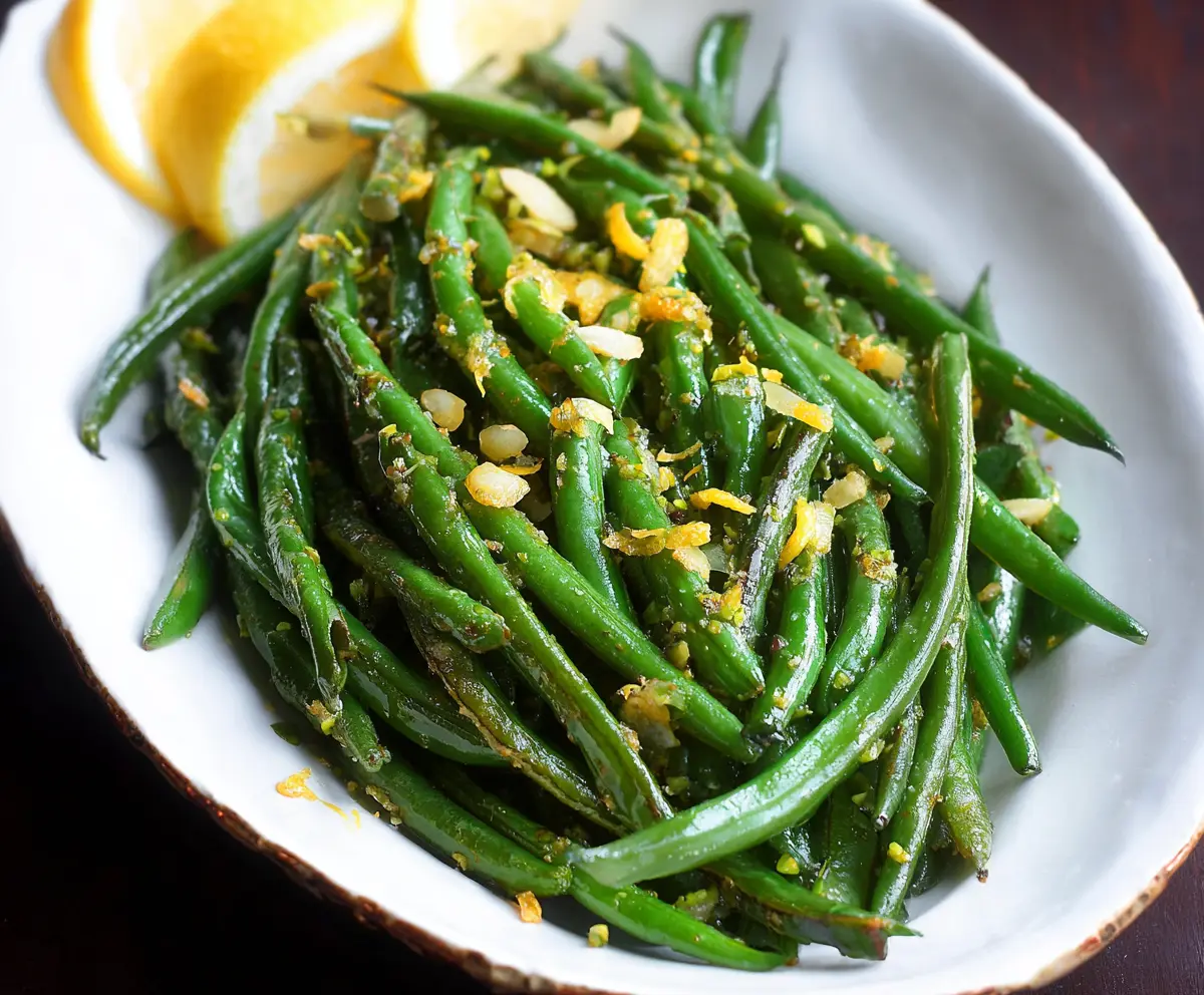Vibrant lemon green beans garnished with fresh herbs on a white plate.