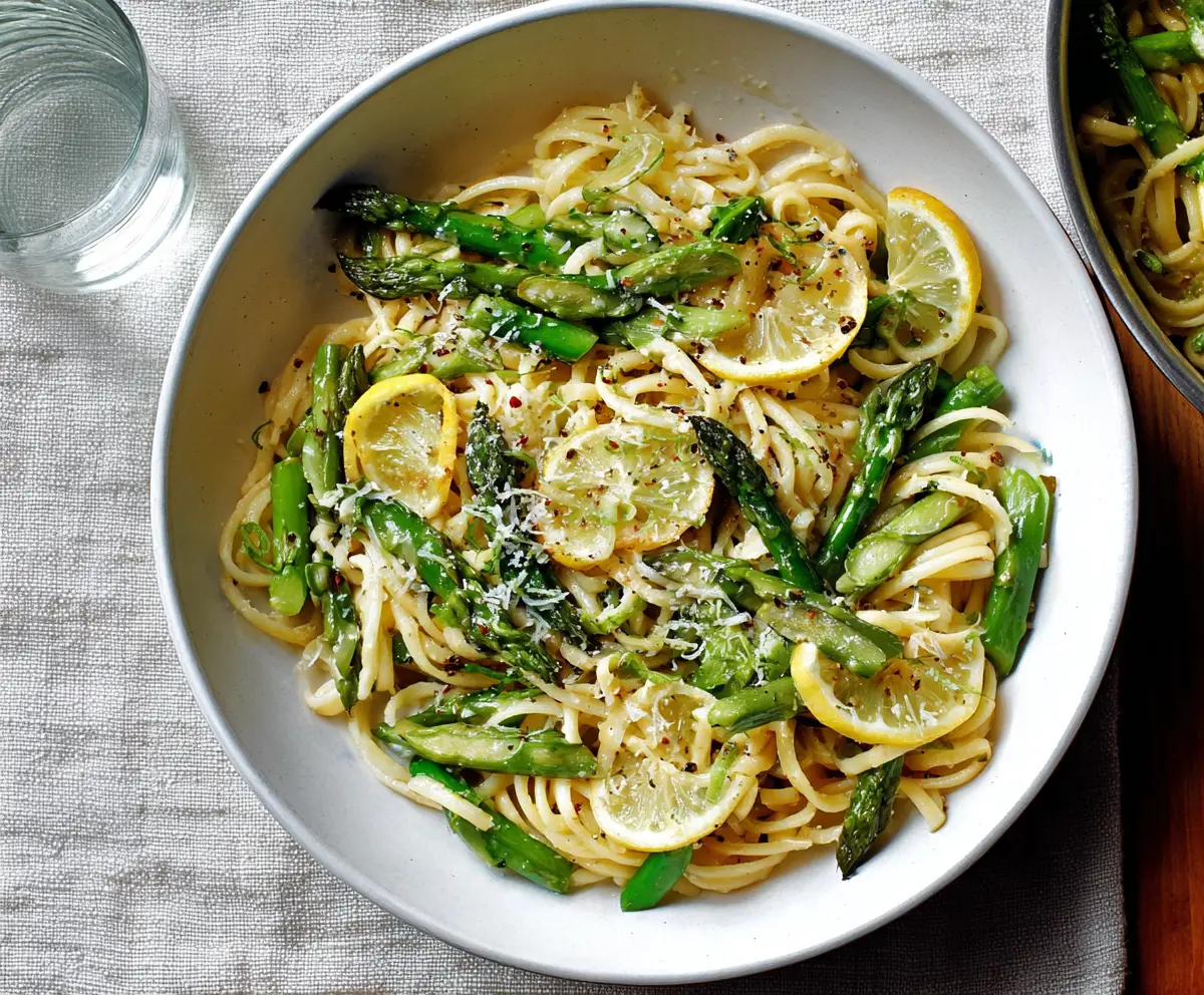 Delicious Lemon Asparagus Pasta garnished with fresh herbs on a white plate.